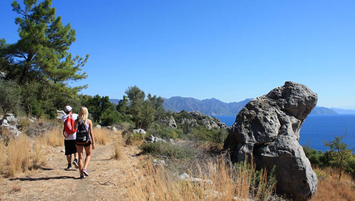 Two hikers on a pine-covered, rocky trail from Possidi to Kalandra in Kassandra, with sea views